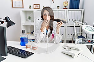 Young dentist woman comparing teeth whitening covering mouth with hand, shocked and afraid for mistake