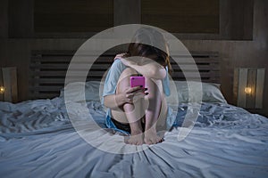 Young depressed Asian Korean girl using mobile phone crying on bed at night feeling sad and depressed victim of cyber bullying or