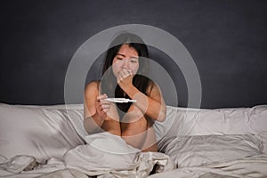 Young depressed and desperate Asian Korean woman crying and scared testing positive result on pregnancy test alone in bed feeling