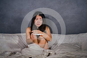 Young depressed and desperate Asian Korean woman crying and scared testing positive result on pregnancy test alone in bed feeling