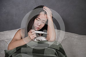 Young depressed and desperate Asian Korean woman crying and scared testing positive result on pregnancy test alone in bed feeling