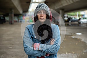 Young depressed homeless girl or woman standing alone under the bridge on the street on the cold weather feeling anxious abandoned