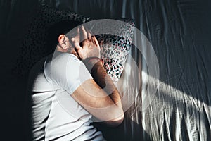 Young depressed man crying in bed