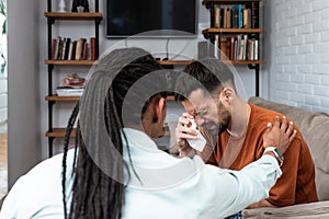 Young depressed man crying talking to mental health counselor during a session in the office. Stressed male at psychotherapy after