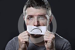 Young depressed man lost in sadness and sorrow holding paper with sad mouth in depression concept photo