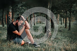 Young depressed man sitting alone in the woods