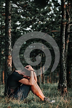 Young depressed man sitting alone in the woods