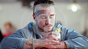 Young depressed man sitting at bar counter drinking cocktail and thinking. Portrait of frustrated Caucasian tattooed