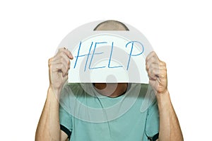 Young depressed man suffering from anxiety and feeling miserable holding help sign on paper in his hands and leaning on the white