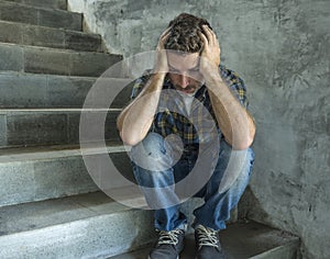 Young depressed and sad man sitting alone outdoors on dark street staircase suffering depression problem looking worried thinking