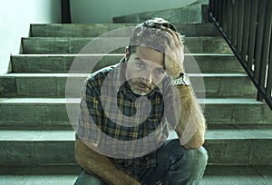 Young depressed and sad man sitting alone outdoors on dark street staircase suffering depression problem looking worried thinking