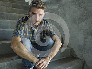 Young depressed and sad man sitting alone outdoors on dark street staircase suffering depression problem looking worried thinking