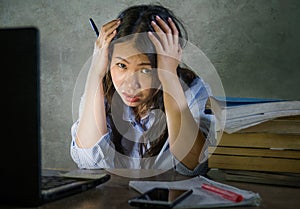 Young depressed and stressed Asian Chinese student girl working with laptop and book pile overwhelmed and frustrated preparing exa