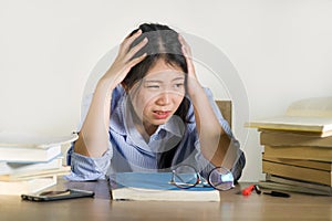 Young depressed and stressed Asian Korean student girl working with laptop and book pile overwhelmed and frustrated preparing exam