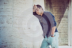 Young depressed and tired man outdoors leaning with one arm on a white wall. Casual dress