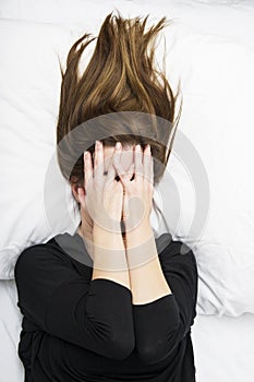Young depressed woman is lying in her bed, covering her face with her hands.