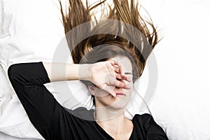 Young depressed woman is lying in her bed, covering her face with her hands. photo