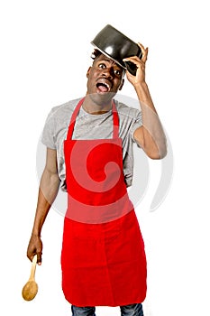 Young desperate and confused black afro american man in chef apron holding cooking pot in his head