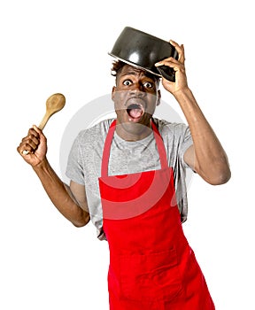 Young desperate and confused black afro american man in chef apron holding cooking pot in his head