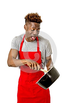 Young desperate and confused black afro american man in chef apron holding cooking pot and spoon in his hands looking lost