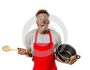 young desperate and confused black afro american man in chef apron holding cooking pot and spoon in his hands looking lost