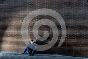 Young desperate jobless man who lost job lost in depression sitting on ground street corner