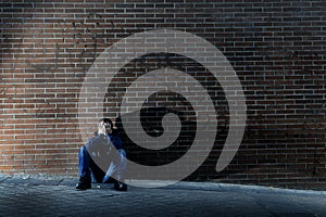 Young desperate man who lost job lost in depression sitting on ground street corner