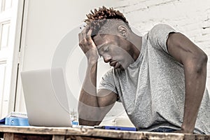 Young desperate and overwhelmed black afro American student man in stress at home working stressed with laptop computer worried an photo