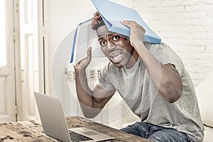 Young desperate and overwhelmed black afro American student man in stress at home working stressed with laptop computer worried an