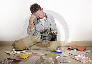 Young desperate and stressed sad man worried holding calculator accounting domestic payments and debt having money problem sitting