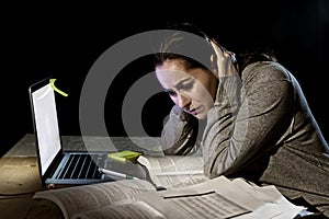 Young desperate university student girl in stress for exam studying with books and computer laptop late at night