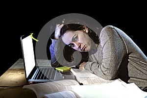 Young desperate university student girl in stress for exam studying with books and computer laptop late at night