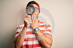 Young detective man looking through magnifying glass over isolated background cover mouth with hand shocked with shame for