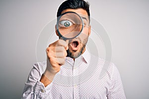 Young detective man looking through magnifying glass over isolated background scared in shock with a surprise face, afraid and