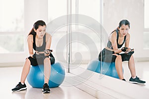 Young, determined Asian woman exercise alone at home gym or sports club, sit on fitness ball with mirror