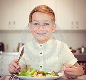 Young diligent boy at a table eating healthy meal with cutlery