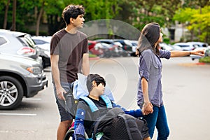 Young disabled boy in wheelchair being wheeled across parking lo