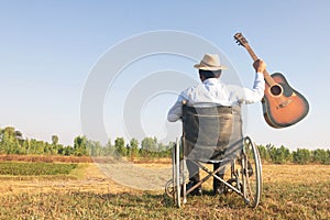 Young disabled man and field background. He is raising guitar and looking into sky