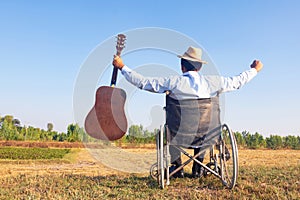 Young disabled man and field background. He is raising guitar and looking into sky