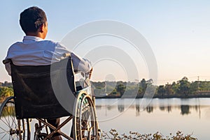 Young disabled man with field background.He is wearing a hat and sitting on wheelchair.