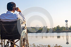 Young disabled man with field background.He is wearing a hat and sitting on wheelchair.