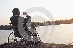 Young disabled man with field background.He is wearing sitting on wheelchair