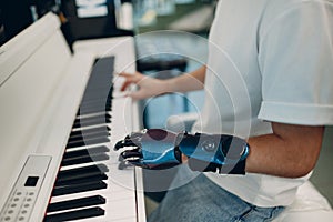 Young disabled man play on piano electronic synthesizer with artificial prosthetic hand in music shop.