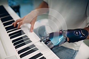 Young disabled man play on piano electronic synthesizer with artificial prosthetic hand in music shop.