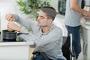 Young disabled man seasoning saucepan on hob