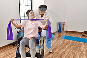 Young disabled woman sitting on wheelchair making mobility exercise using elastic band at the clinic