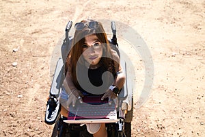 young disabled woman in wheelchair and reduced mobility with her laptop computer teleworking in the park