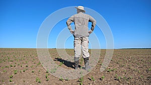 Young disappointed farmer looking at small sprouts of sunflower on the field and feeling threat of a crop failure in