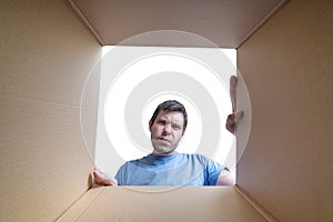 Young disappointed man is looking on gift inside cardboard box