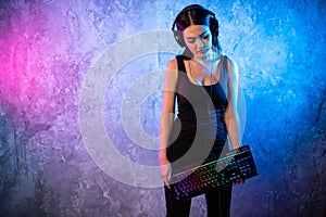 Young Disco Girl Wearing Gaming Headset Holding Gaming Kyeboard. Room Lit in Retro, Retrowave or Cyberpunk Style